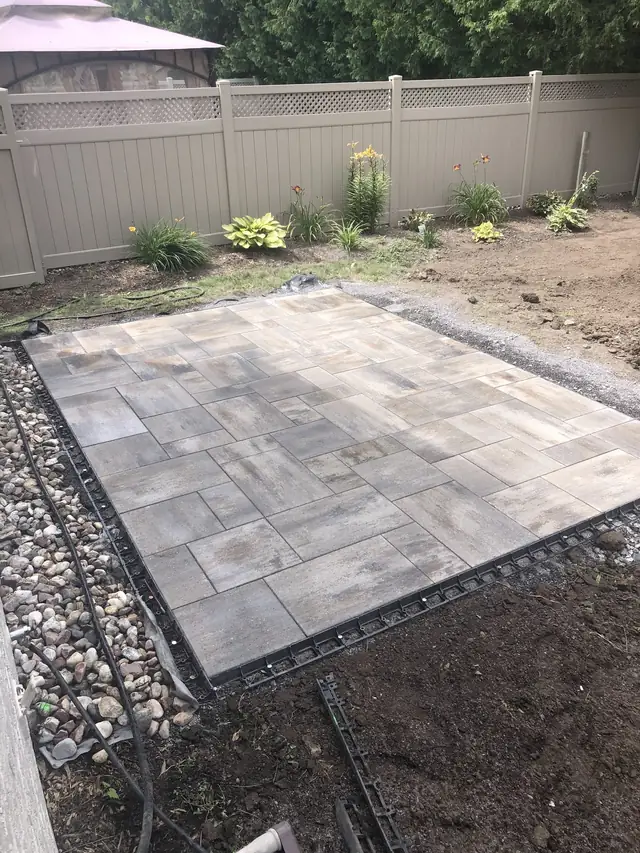A rectangle of freshly laid grey pavers on a gravel base in a backyard
