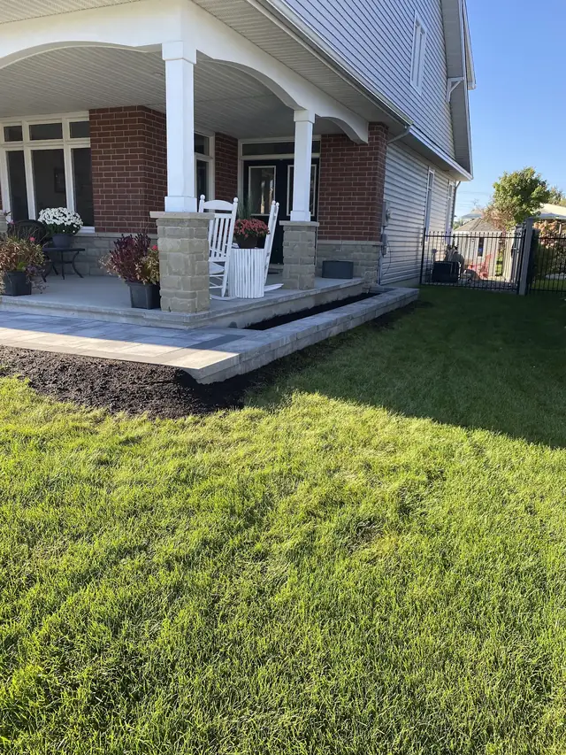 A covered front porch with white columns, a stone landing and paver edging along the lawn