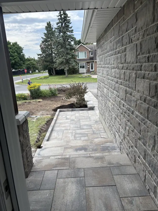 A narrow interlock walkway running between a stone-faced wall and a garden bed